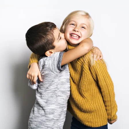 A little boy affectionately hugging a little girl, who laughs at the camera