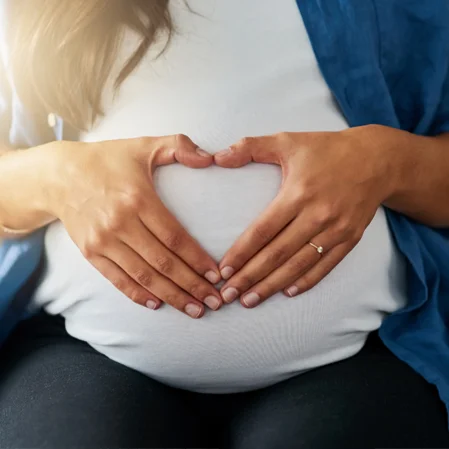 A woman's hands created a heart shape over her pregnant belly
