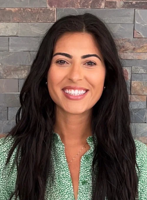 Dr. Gina Caira standing against a brick wall and smiling